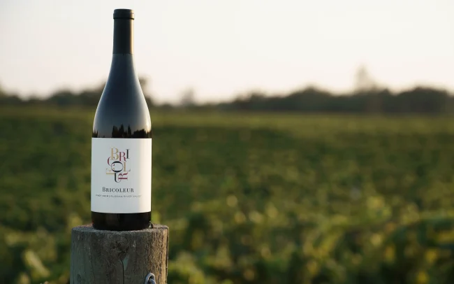 Bottle of Bricoleur Vineyards wine on top of a vineyard post